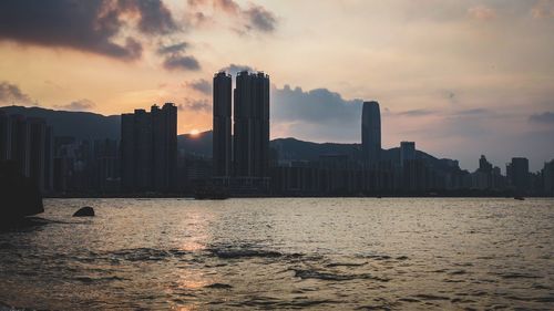 Sea by cityscape against sky during sunset