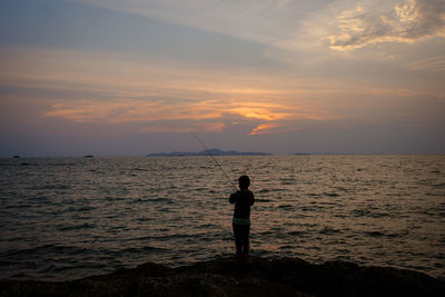 Silhouette woman standing at beach against sky during sunset