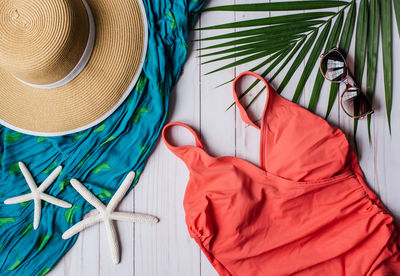 Top view of swimsuit and beach accessories on white wood background.