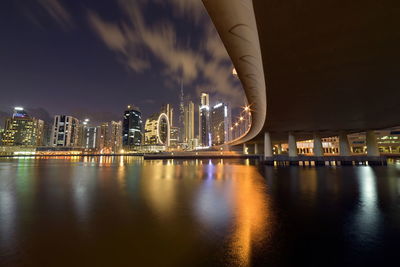 Illuminated city by river against sky at night