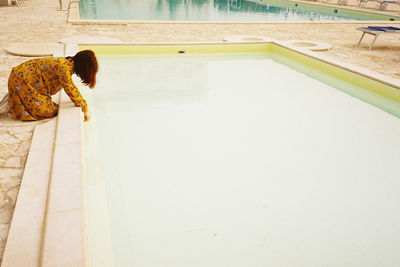 Side view of woman putting hand in swimming pool