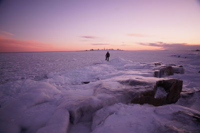 Silhouette man walking on snow covered landscape against sky during sunset