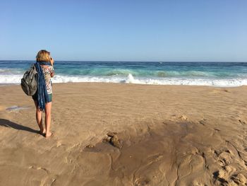 Rear view of woman standing on beach against clear sky