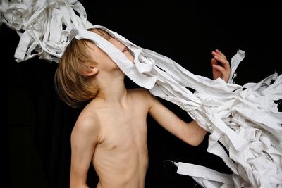 Shirtless boy throwing white fabric against black background