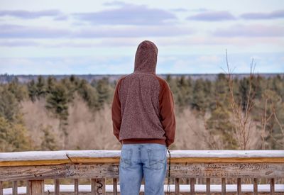 Rear view of man standing on railing against sky