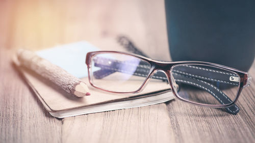 Close-up of eyeglasses with pencil and book on table