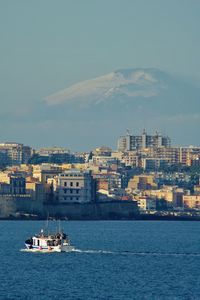 Sailboats in sea by buildings against sky