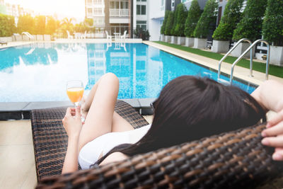 High angle view of woman with juice sitting by swimming pool in city