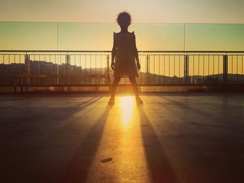 Girl standing against railing during sunset