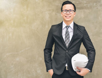 Portrait of smiling young engineer with hardhat against wall