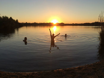 Silhouette ducks swimming in lake against sky during sunset