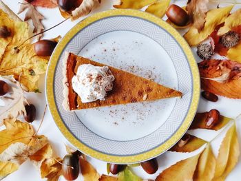 Pumpkin pie with whipped cream surrounded by fall leaves.