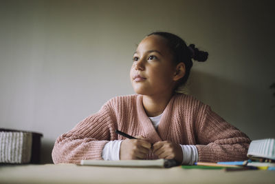 Thoughtful girl day dreaming while coloring at home