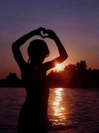 Silhouette woman standing by water against orange sky