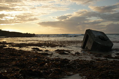 Rock at beach against sky during sunset