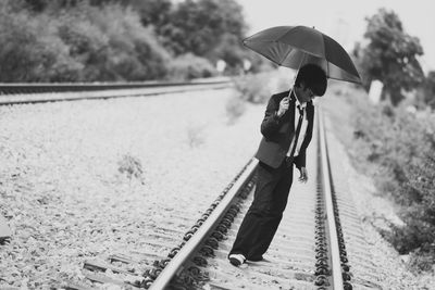 Businessman with umbrella walking on railroad track