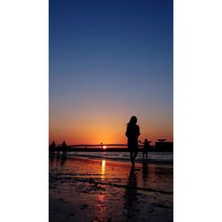 Silhouette people standing on beach against clear sky during sunset