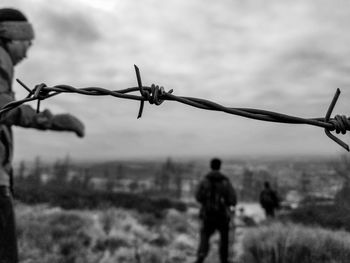 Close-up of barbed wire fence on field against sky