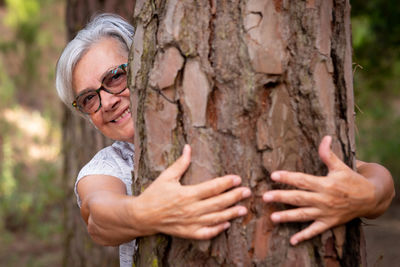 Portrait of woman with arms raised on tree trunk