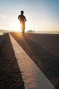Rear view full length of boy jogging on road during sunrise