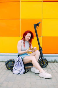 Woman uses a smartphone and an electric scooter in the summer in the city