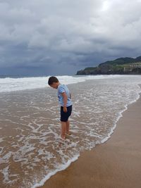 Child standing on beach against sky