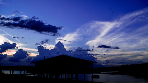 Silhouette house and buildings against sky at sunset