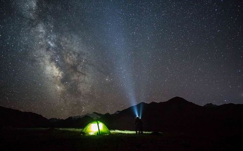 Silhouette people by illuminated tent against star field