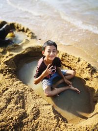 Portrait of smiling boy sitting on wet sand at beach