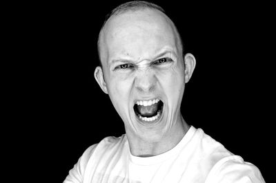 Close-up portrait of man screaming against black background