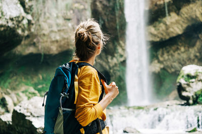 Young active unrecognizable woman from behind with a backpack looking at a waterfall in a canyon.