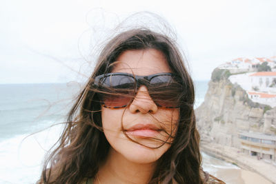 Close-up portrait of young woman wearing sunglasses against beach