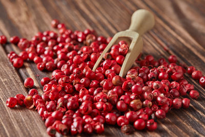 Red peppercorns with wooden spatula scattered on wooden vintage background