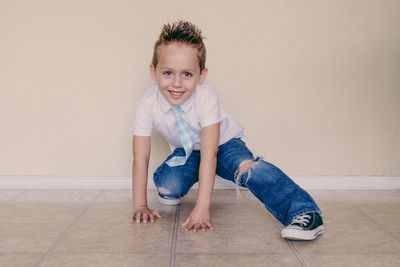 Portrait of cute boy crouching on tiled floor against wall