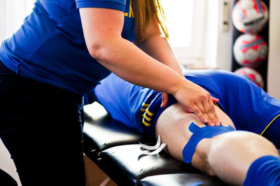 Midsection of woman applying bandage on sport player thigh