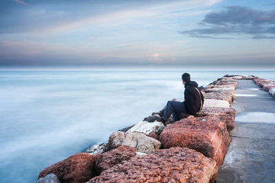 Man on rock by sea against sky during sunset