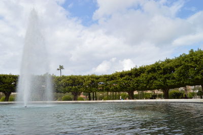 Fountain in lake at park against cloudy sky