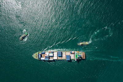 Aerial top view container ship and tugboat dragging floating in green sea, business and industry 