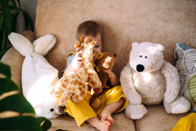 Funny little child is having fun, playing with soft toys on the couch at home.