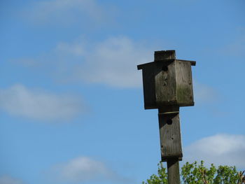 Low angle view of birdhouse on wooden post against sky