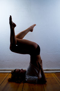 Side view of woman exercising on floor against wall
