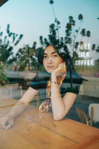 Portrait of young woman sitting in cafe seen through window