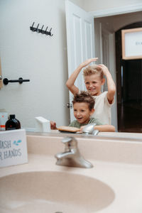 Portrait of smiling boys  in bathroom brushing their hair 