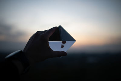 Cropped hand holding crystal against sky during sunset