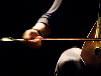 Midsection of man playing string instrument against black background