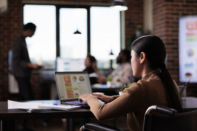 Businesswoman using laptop sitting on wheelchair at office