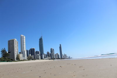 Modern buildings by sea against clear blue sky