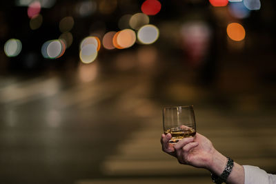 Close-up of hand holding alcohol glass on street at night