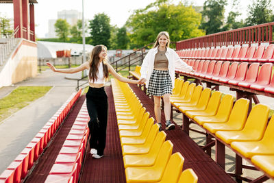 Two teenage girls walk together through the stands of the school stadium, talking, holding hands