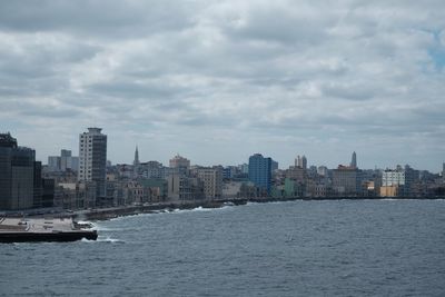 Sea by buildings in city against sky